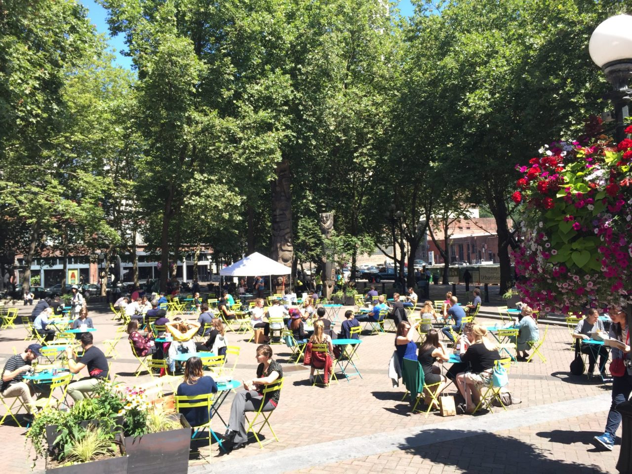 People sit at colorful tables in a park square.
