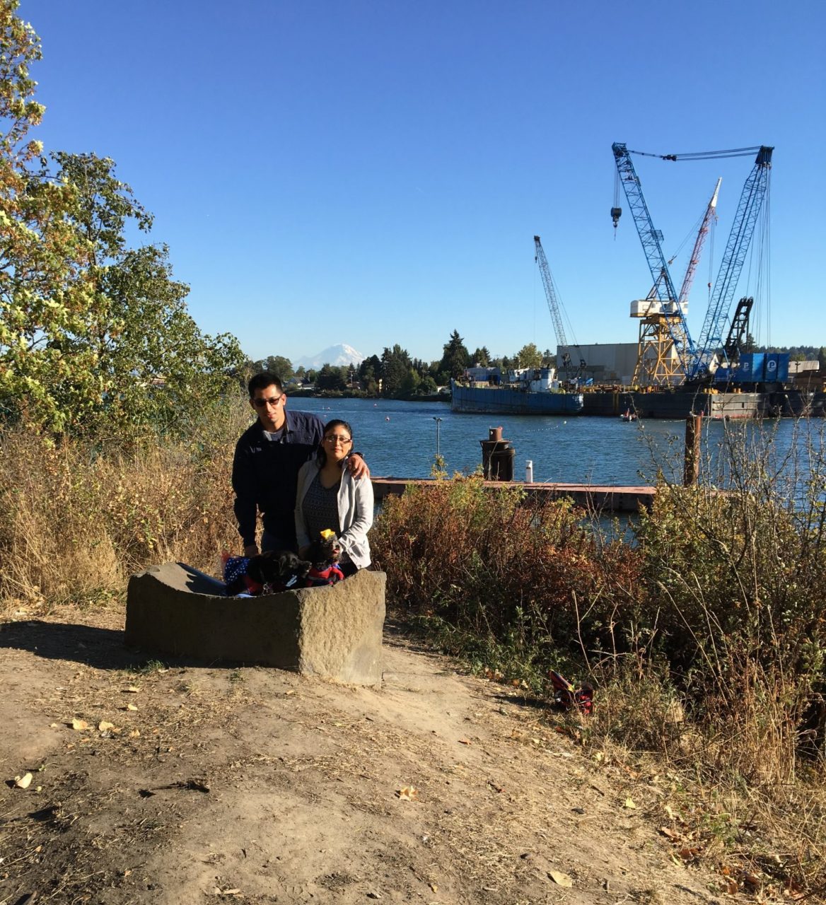 Two people pose next to rock boulder on river bank.